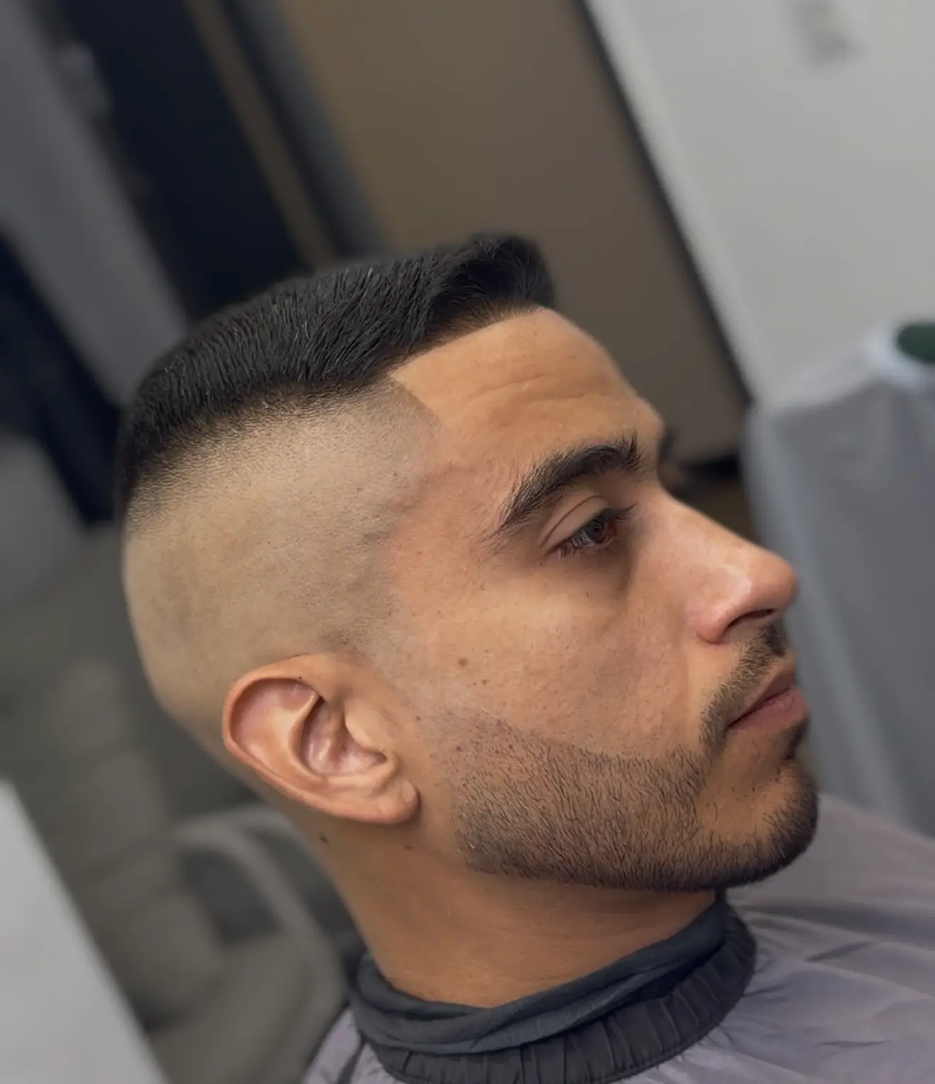 Close side profile of a short combed top with a high skin fade and shaped beard