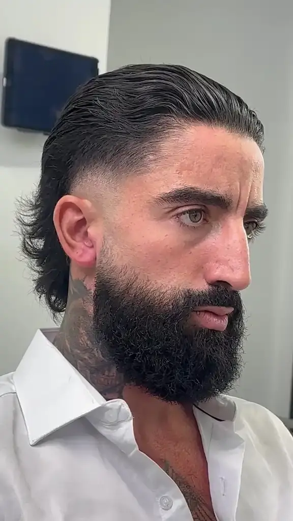 Slicked-back hair with a low fade and full beard, shown in side profile